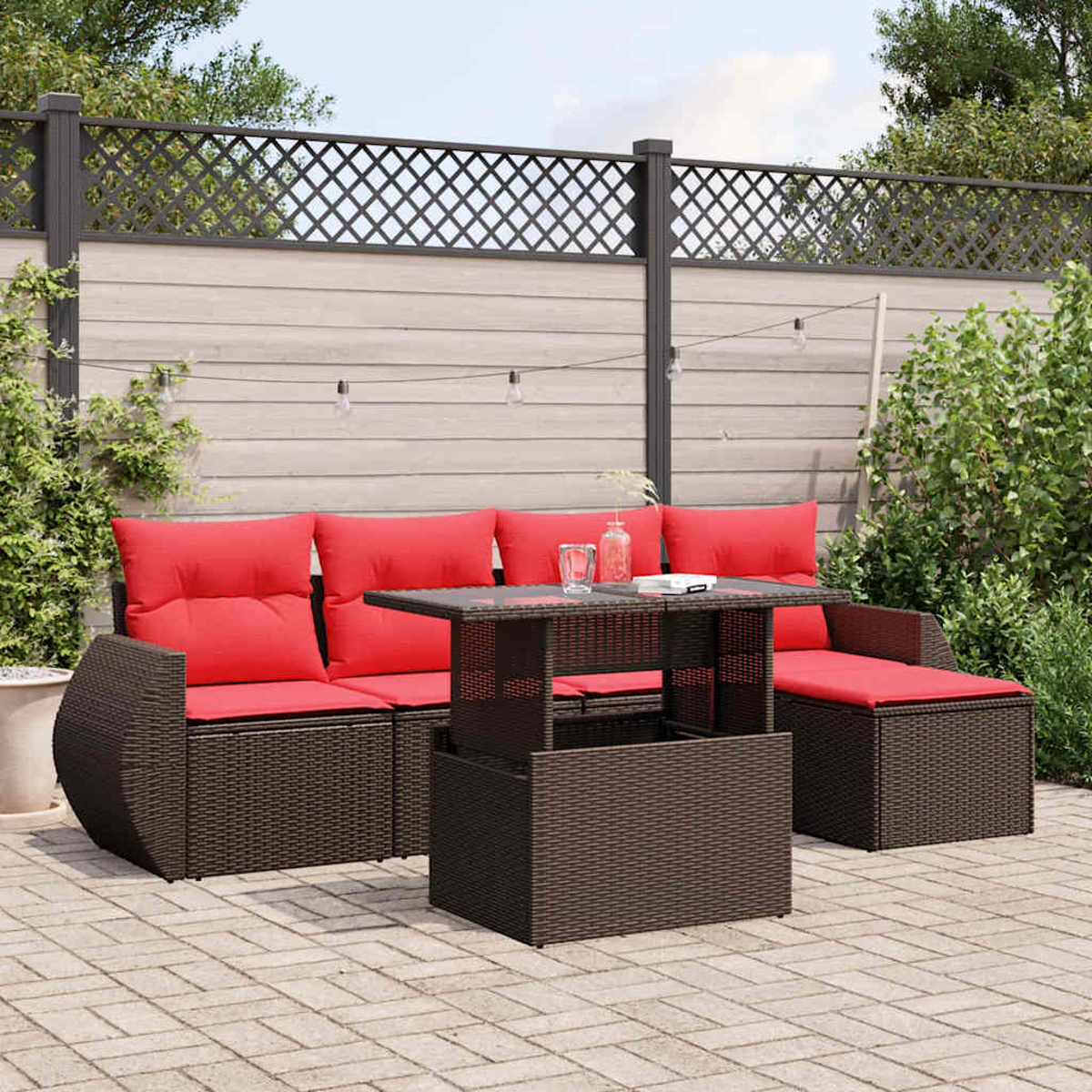 Juego de muebles de exterior con cojines rojos. Una mesa con tapa de cristal frente al sofá. El fondo tiene valla y vegetación.
