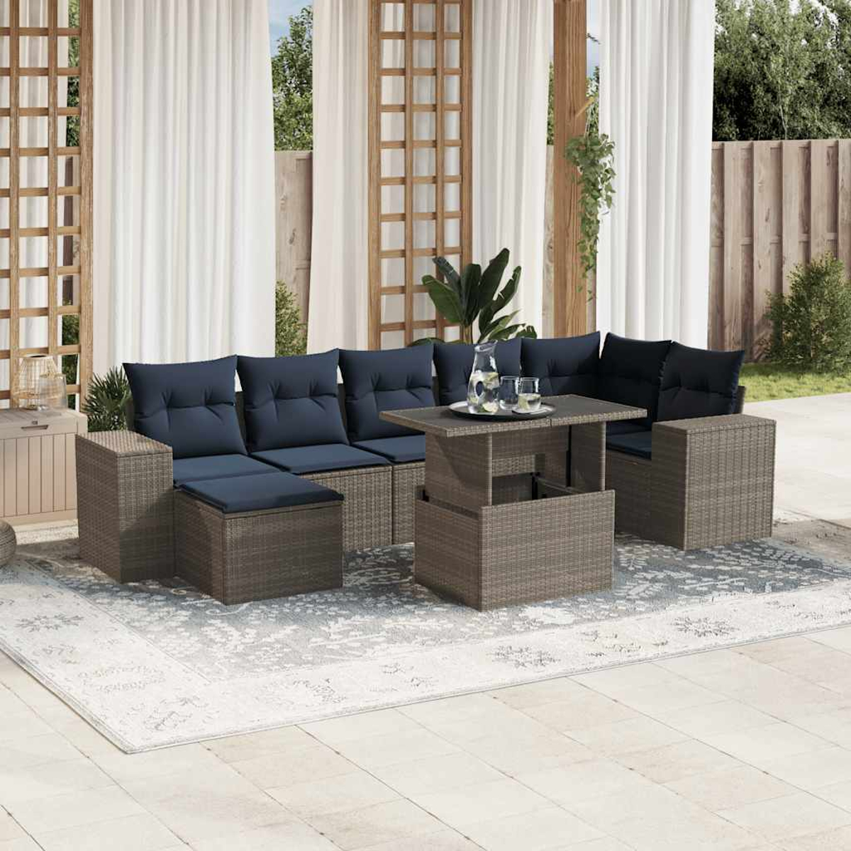 Garten-Sitzgruppe mit marineblauen Kissen, einem Tisch mit Hubfunktion und einem Teppich. Weiße Vorhänge und ein Holzgitter im Hintergrund.