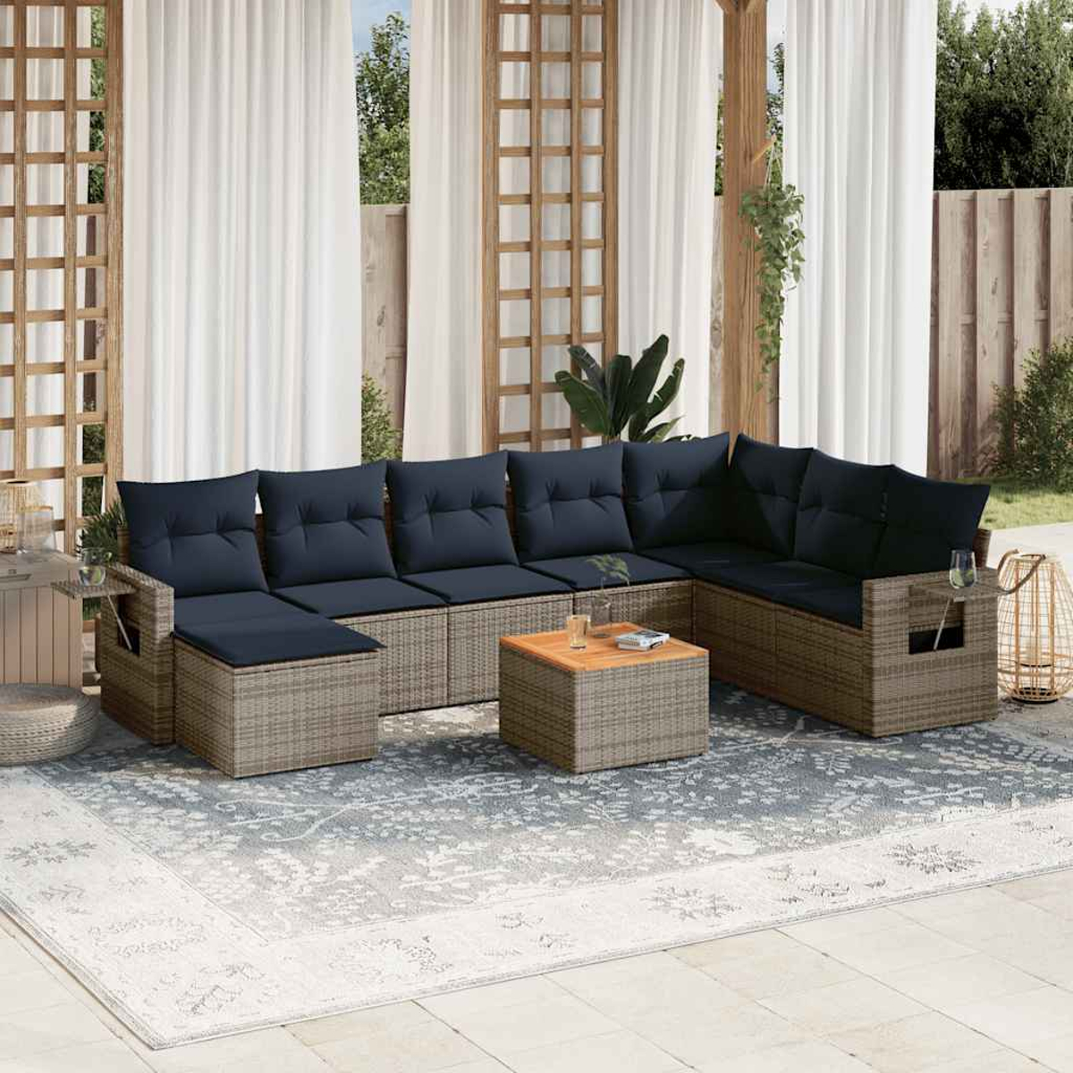 Sofá seccional exterior con cojines azul marino. Una mesa de centro y una alfombra están al frente. Cortinas transparentes y un enrejado de madera al fondo.
