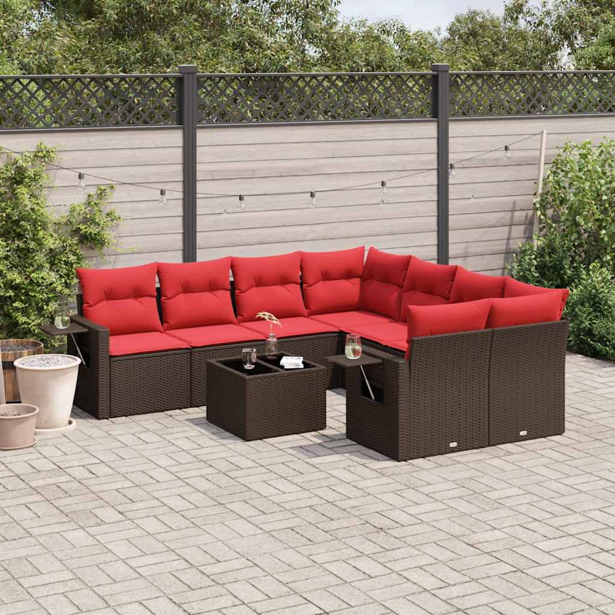Garten-Terrassenset: braune Korbmöbel mit roten Kissen. Enthält ein Ecksofa und zwei kleine Tische auf einer gepflasterten Terrasse.
