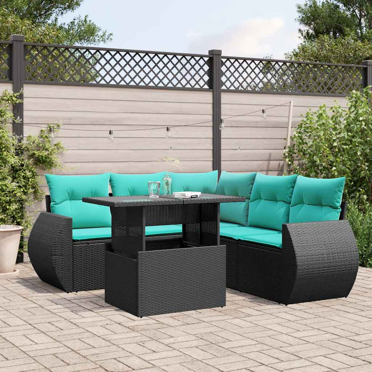 Terrassenmöbel mit schwarzem Korbmöbel, türkisfarbenen Kissen und einem Tisch mit Hebevorrichtung. Im Hintergrund ein Zaun und Grün.