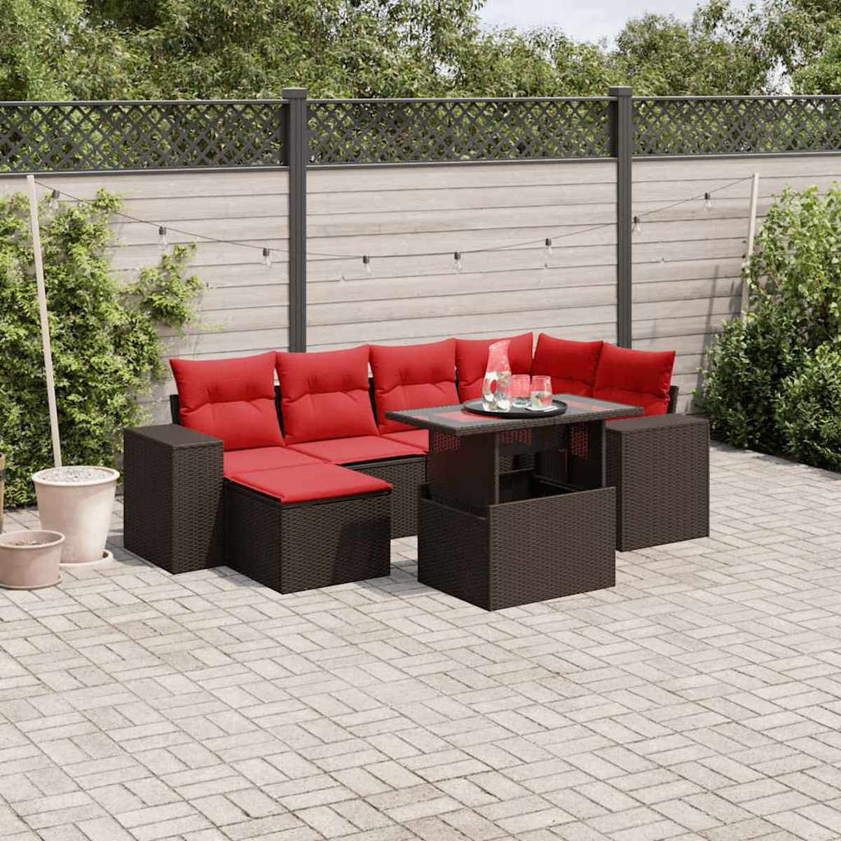 Juego de patio al aire libre con cojines rojos sobre un marco de mimbre marrón oscuro. Una mesa sostiene vasos y una jarra. Patio pavimentado con valla.