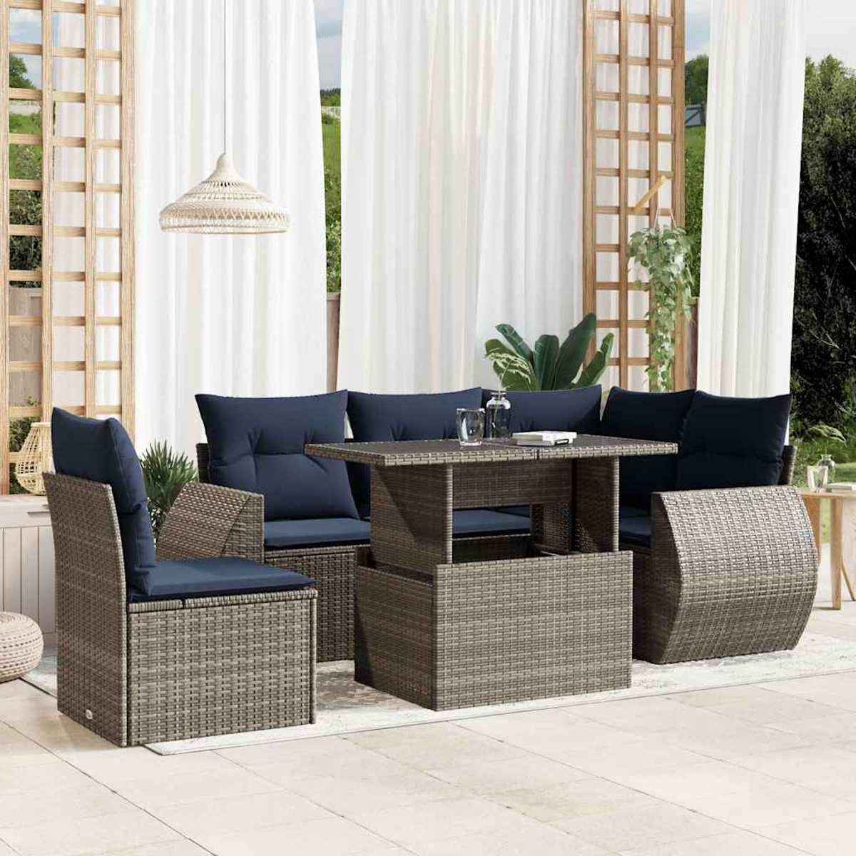 Garten-Set mit grauen Korbmöbeln, marineblauen Kissen und einem Tisch mit Hubfunktion. Weiße Vorhänge und eine gewebte Leuchte.