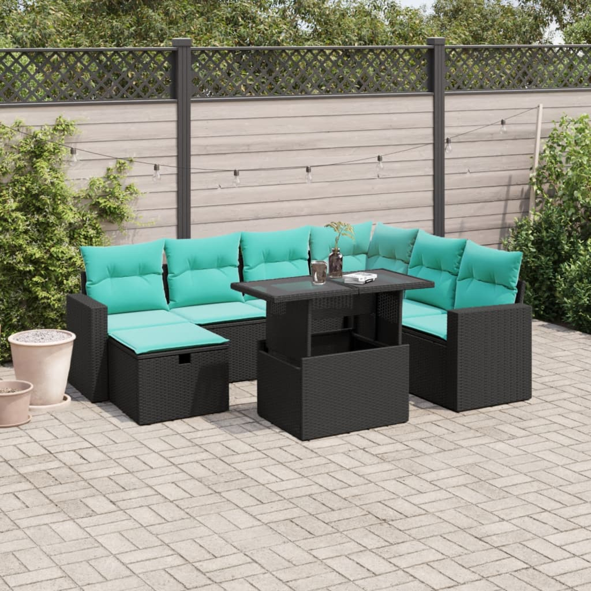Gartenmöbel-Set. Schwarzes Korbgeflecht mit türkisfarbenen Kissen. Tisch mit Glasplatte. Ziegelterrasse und Holzzaun im Hintergrund.