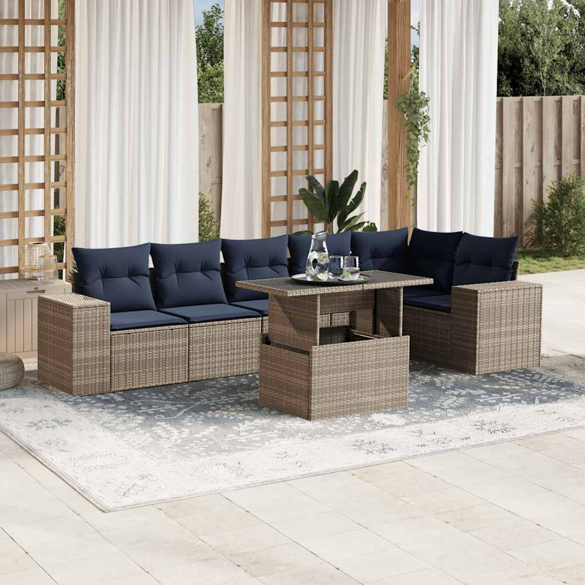 Outdoor-Terrassenset mit blauen Kissen. Tisch und Sitzgelegenheiten stehen auf einem Teppich. Vorhänge, Holzkonstruktion und Pflanzen im Hintergrund.