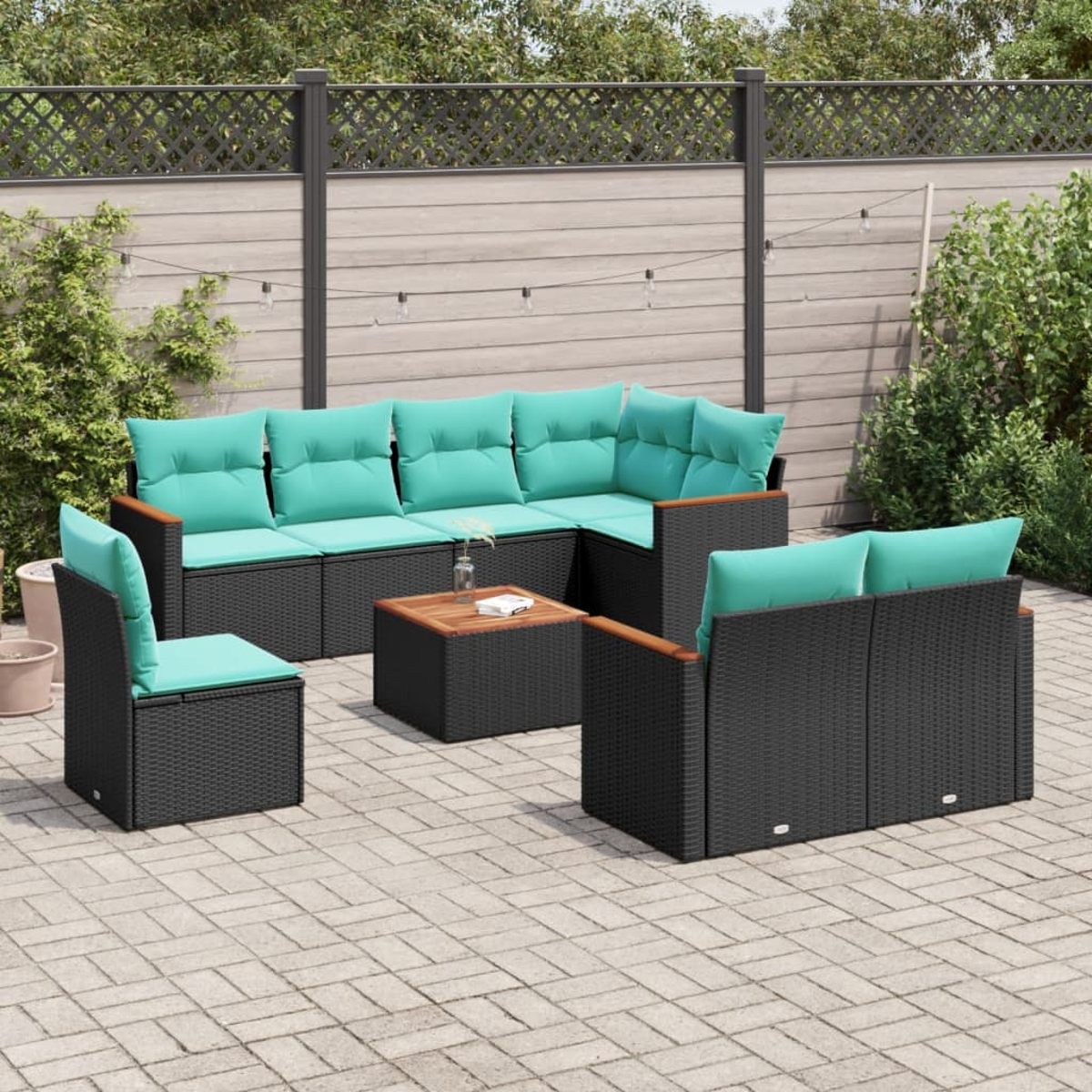 Terrassen-Set mit schwarzem Korbmöbel, türkisfarbenen Kissen und Holztisch auf Ziegelpflaster.