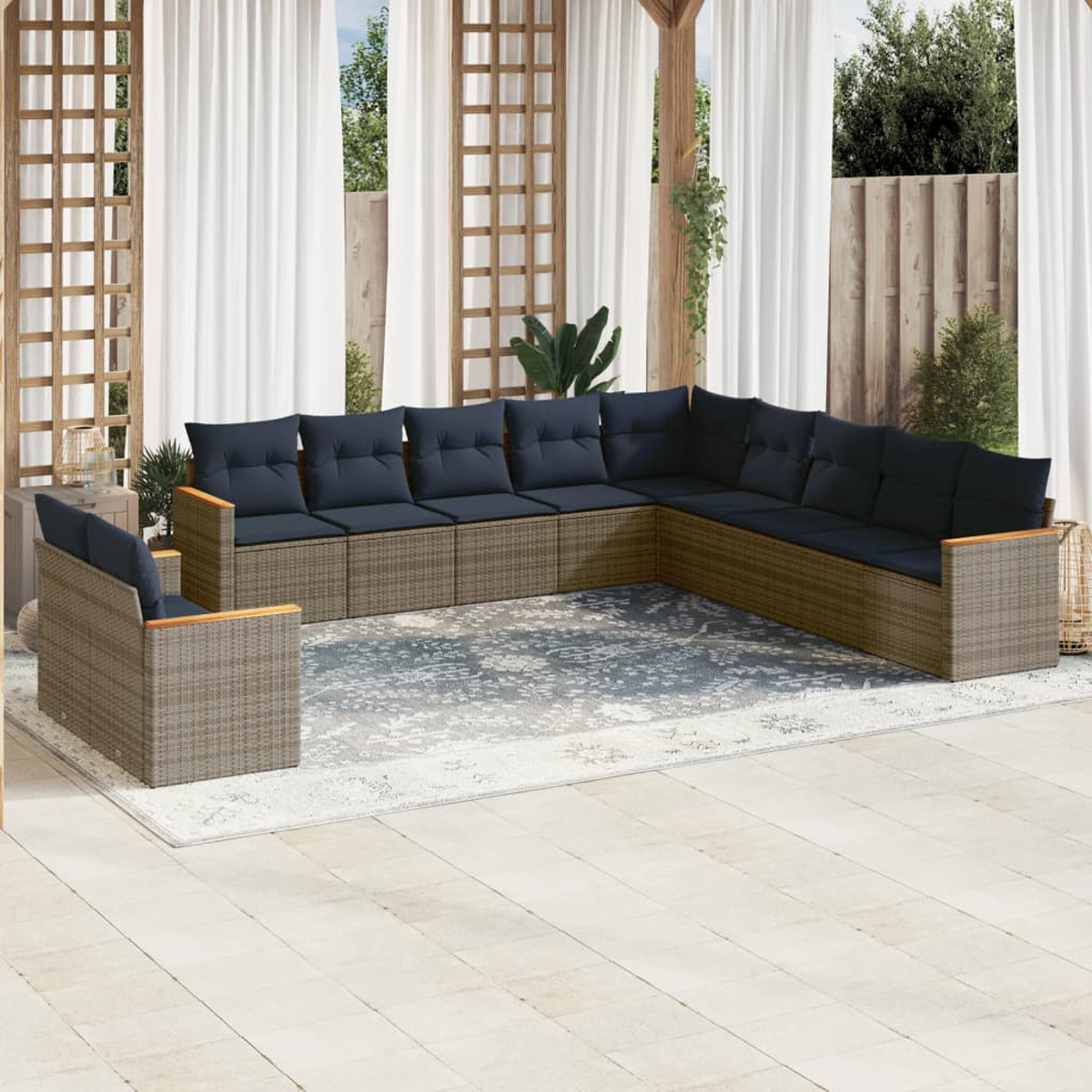 Sofá seccional exterior con cojines azul marino. Una silla a juego está sobre una alfombra. Cortinas blancas y pérgola de madera enmarcan la escena.