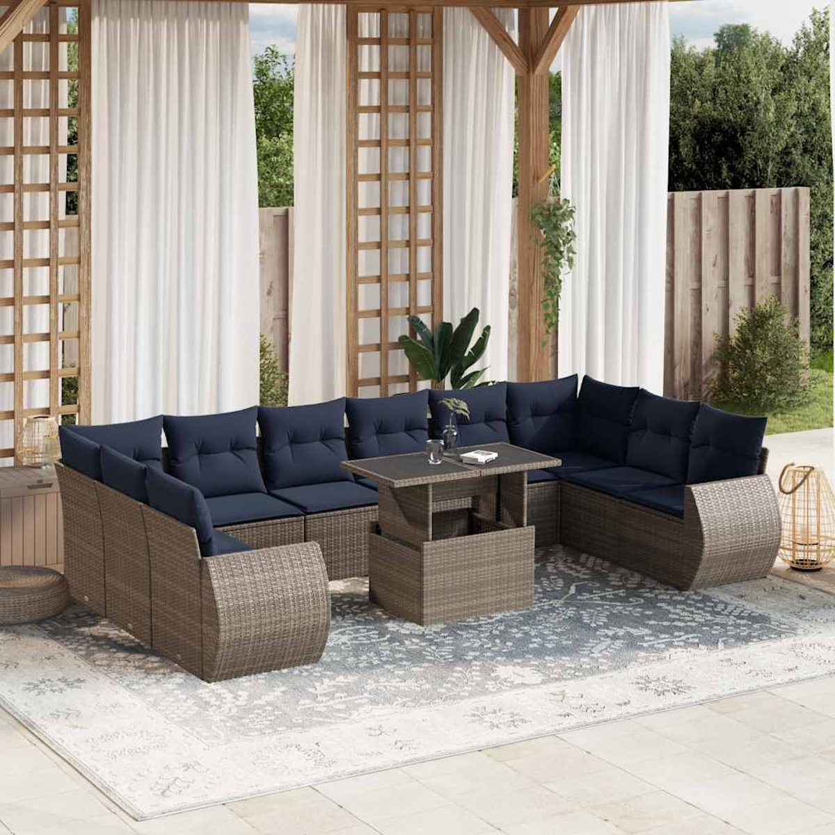 Outdoor-Sitzbereich mit Korbmöbeln, blauen Kissen, einem Tisch und weißen Vorhängen. Im Hintergrund Bäume und ein Holzzaun.