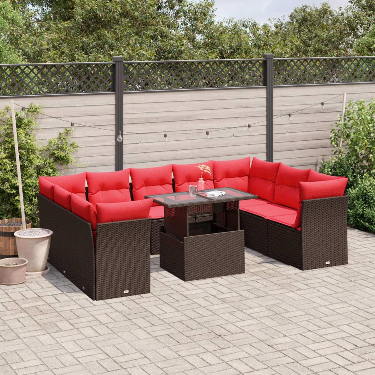 Seccional exterior con cojines rojos y mesa de cristal en patio de ladrillo. Valla de madera y vegetación al fondo.