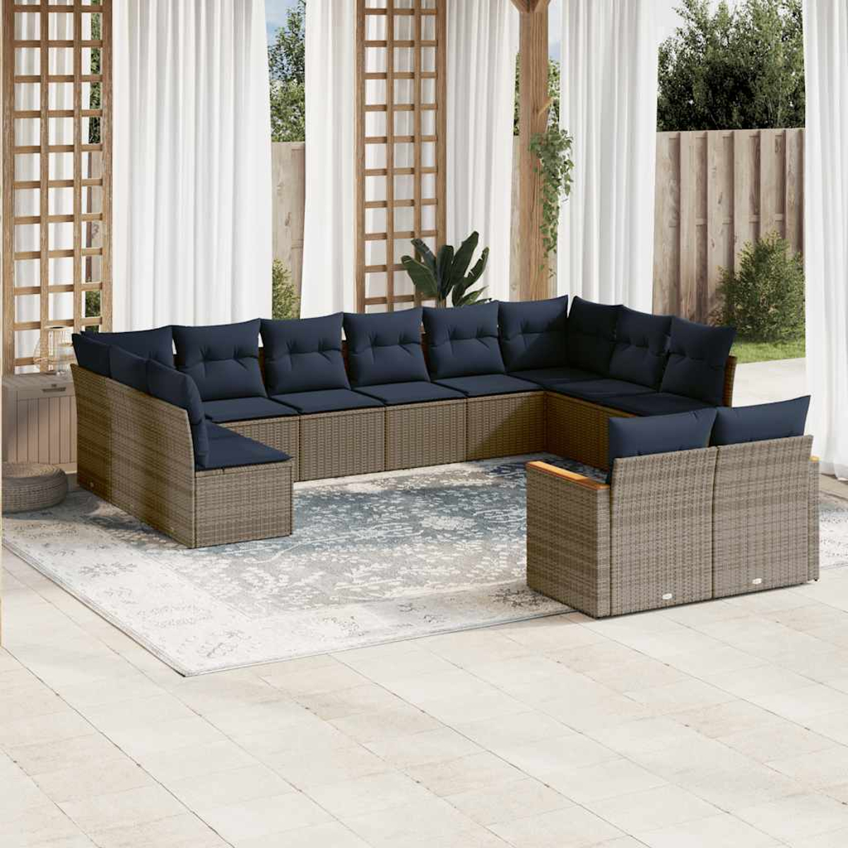 Outdoor-Ecksofa mit marineblauen Kissen. Geflochtener Rahmen auf einem gemusterten Teppich. Weiße Vorhänge und Holzstruktur im Hintergrund.