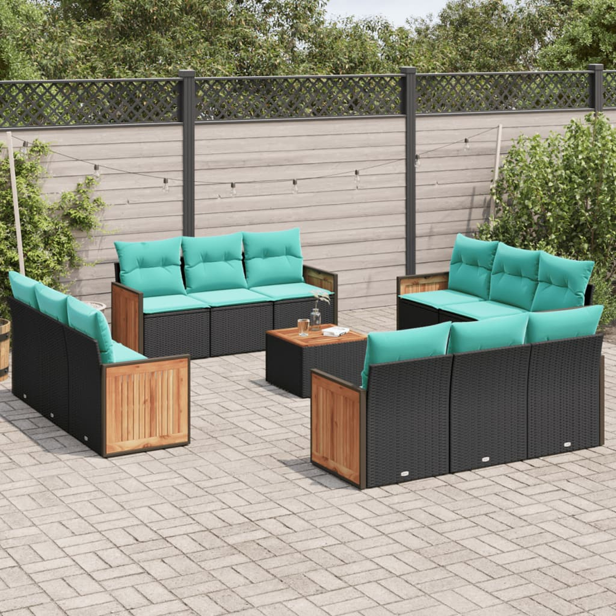 Gartenmöbel-Set mit schwarzem Korbgeflecht, Holzakzenten und türkisfarbenen Kissen. Ein kleiner Tisch steht in der Mitte auf einer Steinterrasse.