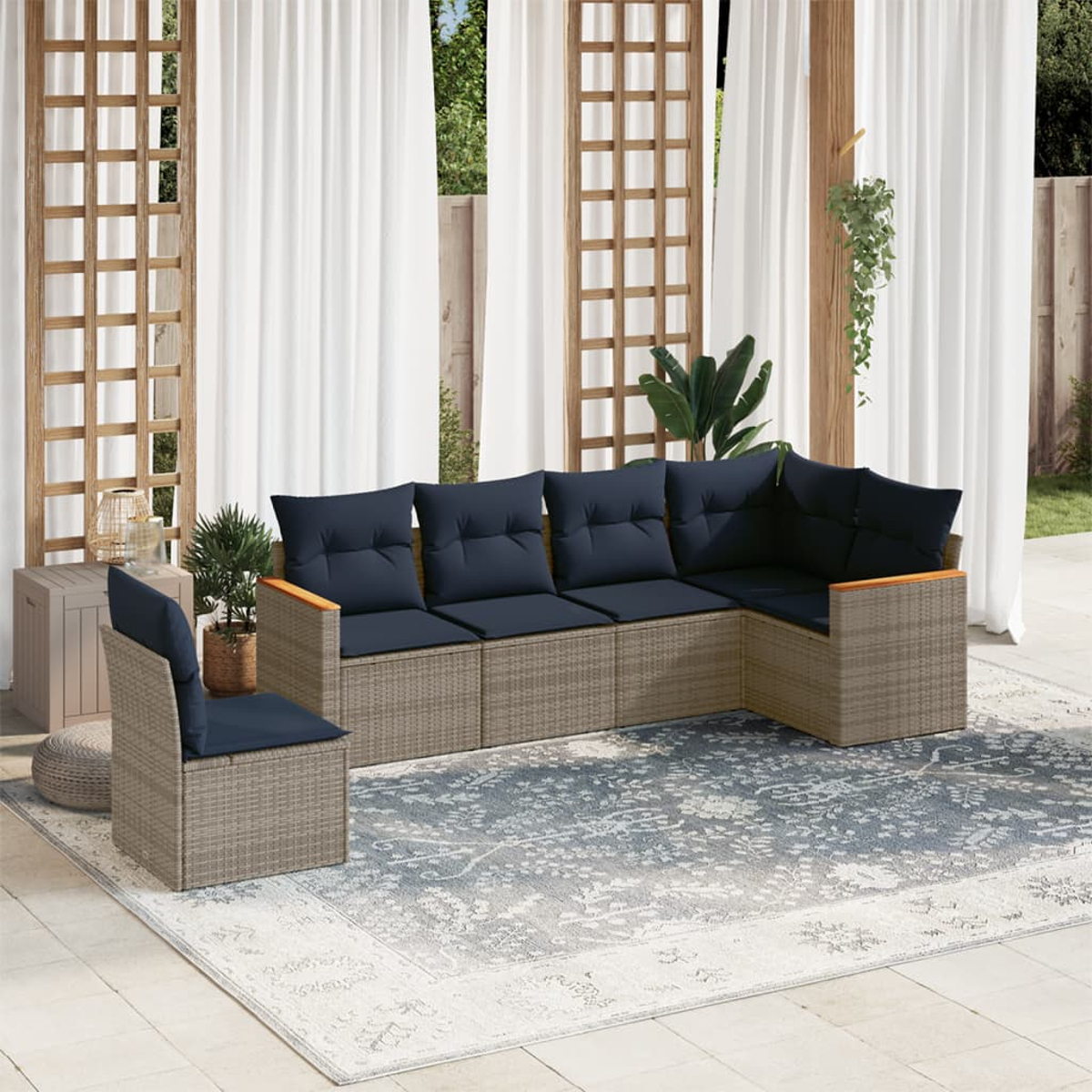 Outdoor-Sitzgruppe mit blauen Kissen auf einem gemusterten Teppich. Weiße Vorhänge und Holzgitter im Hintergrund.