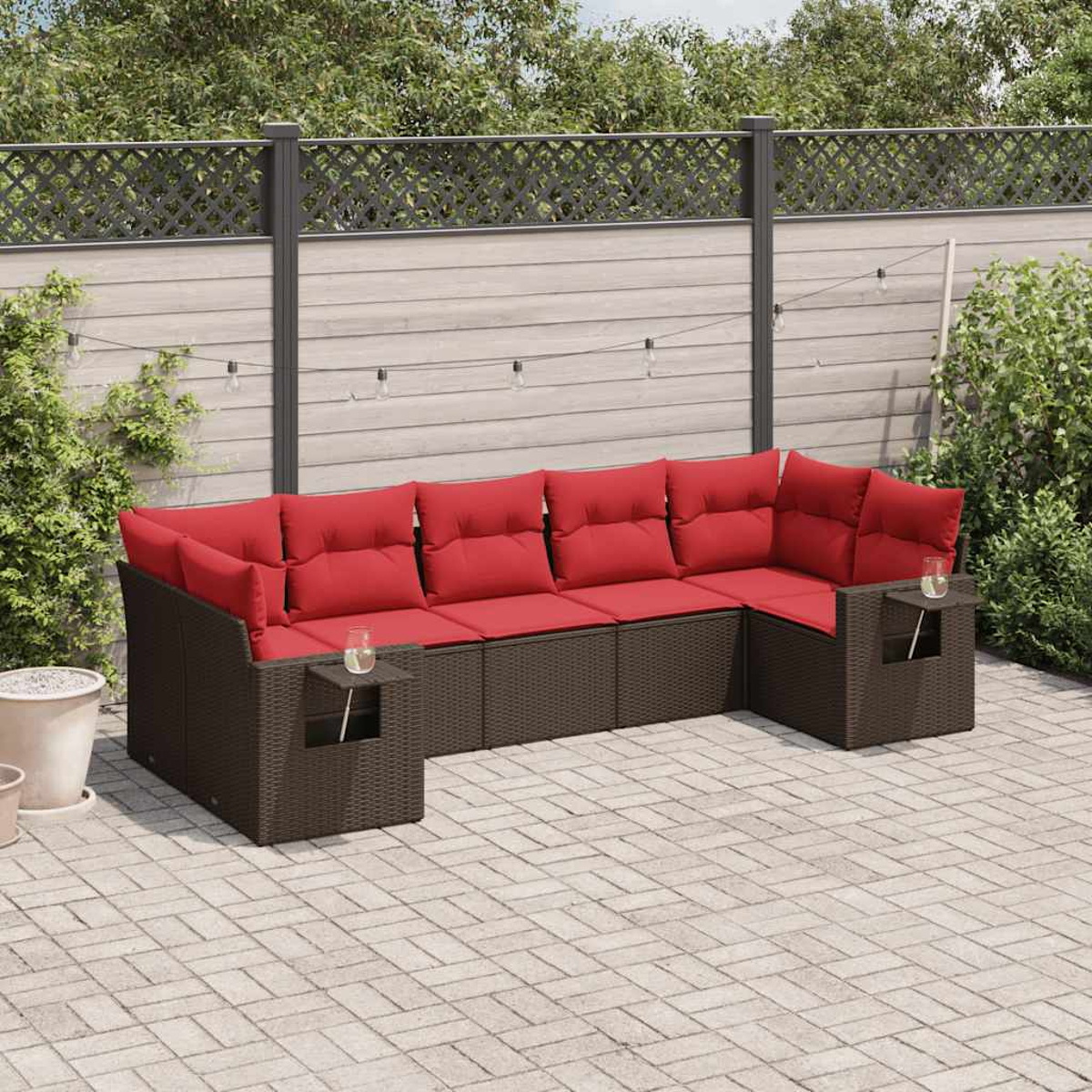 Outdoor-Ecksofa mit roten Kissen auf einer Terrasse. Im Hintergrund befinden sich ein Zaun und Grün. Zwei kleine Tische sind am Sofa befestigt.