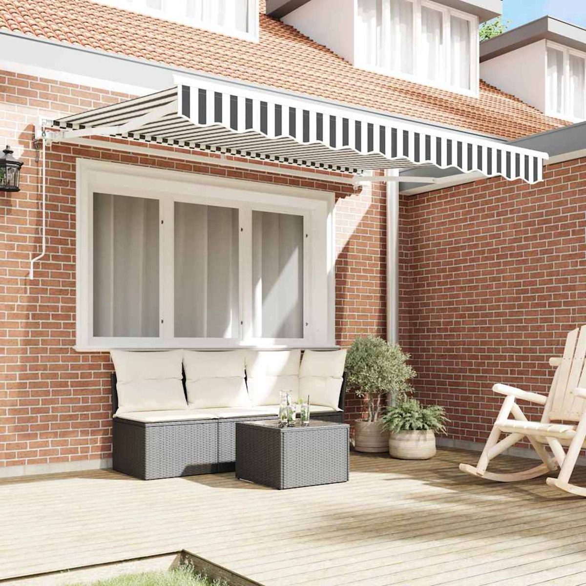 Eine Terrassenszene mit einer schwarz-weiß gestreiften Markise, einer Backsteinmauer, einem Sofa mit Kissen, einem Tisch und einem Schaukelstuhl.