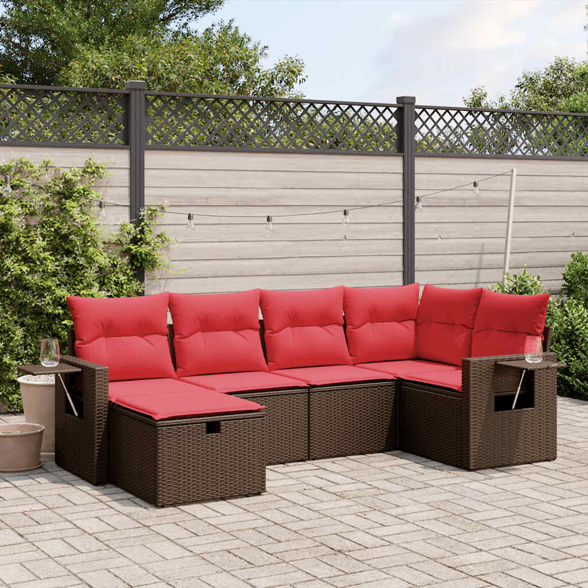 Ein Ecksofa mit roten Kissen im Freien steht auf einer Terrasse. Im Hintergrund sind ein Zaun und Pflanzen. Gläser stehen auf den Beistelltischen.