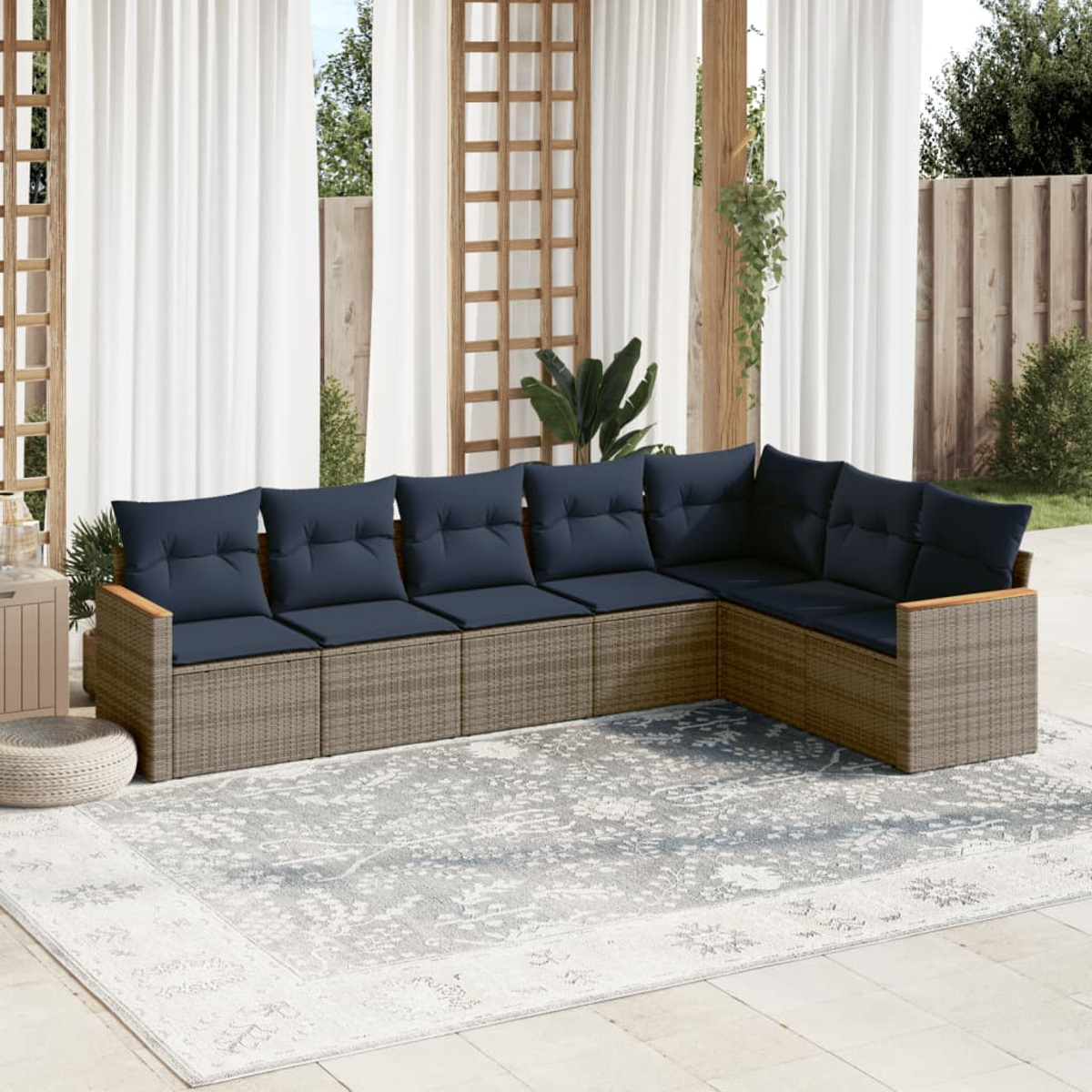 L-förmiges Outdoor-Sofa mit blauen Kissen auf einem gemusterten Teppich, vor weißen Vorhängen und Holzstrukturen.