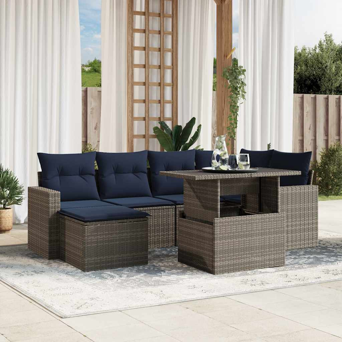 Outdoor-Korbmöbel-Set mit marineblauen Kissen. Ein Tisch mit Hubfunktion trägt ein Tablett mit Gläsern und einer Kanne. Weiße Vorhänge im Hintergrund.