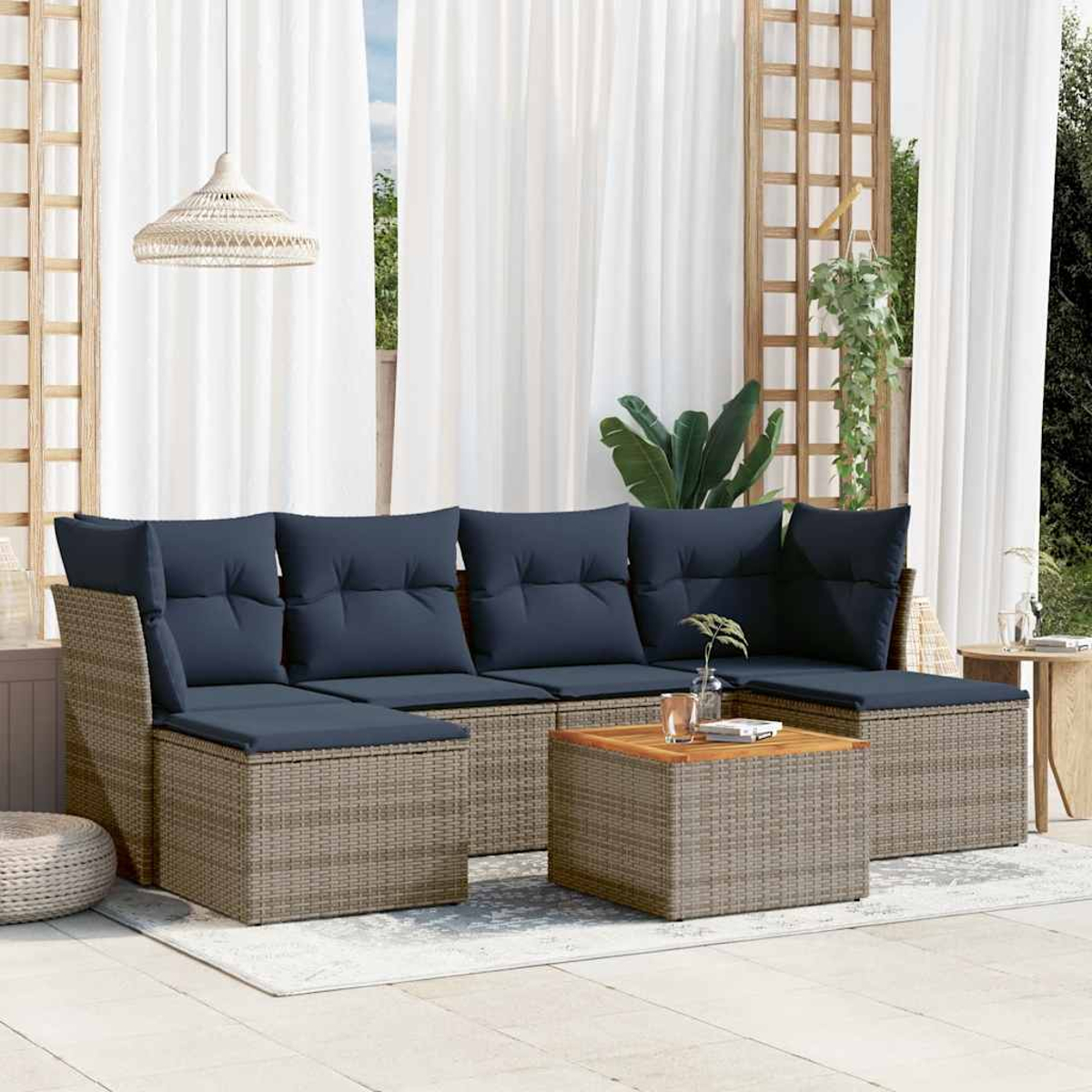 Gartensitzgruppe mit marineblauen Kissen, Korbbasis, Couchtisch. Weiße Vorhänge im Hintergrund, Hängelampe und Pflanzen.
