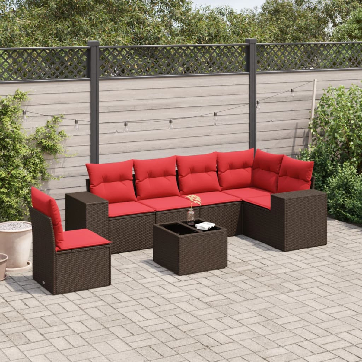 Gartenmöbel-Set mit roten Kissen. Braune Korbmöbel mit Sofa, Stühlen und Tisch. Im Hintergrund ein Holzzaun.