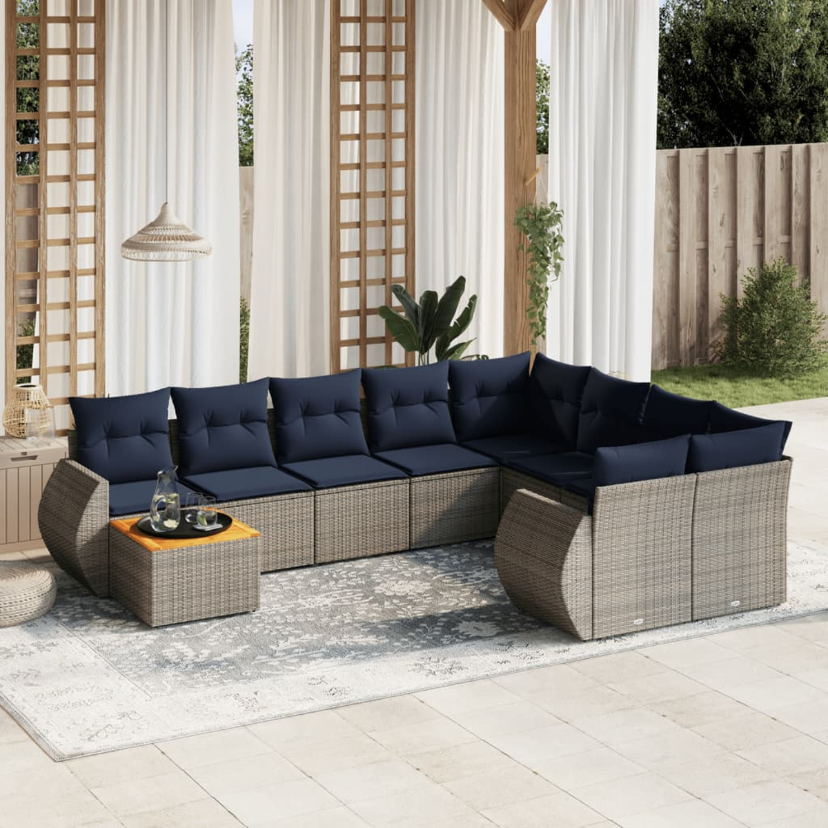 Outdoor-Ecksofa mit marineblauen Kissen auf einem gemusterten Teppich. Ein kleiner Tisch hat Getränke. Weiße Vorhänge, Holzgitter und Pflanzen sind sichtbar.