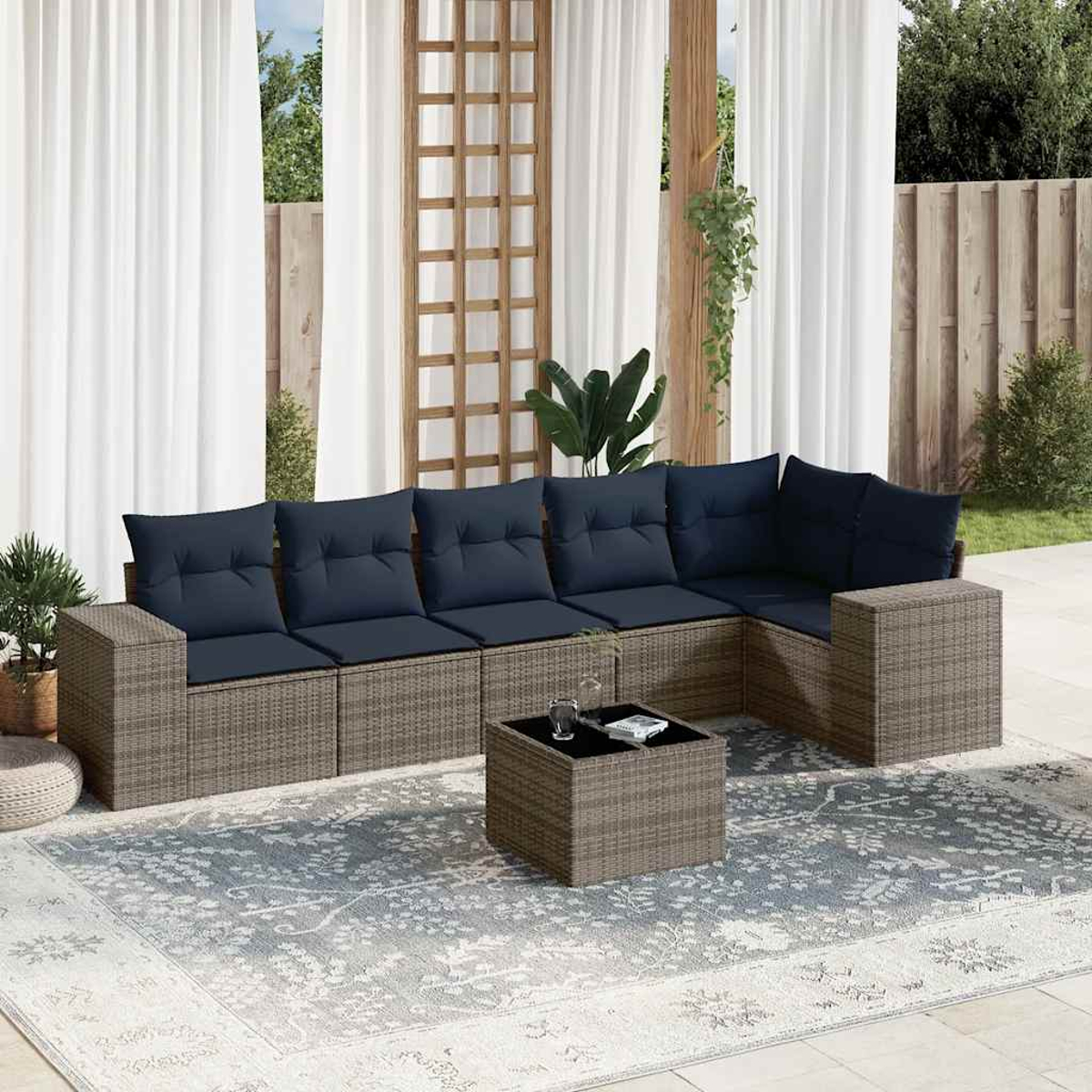 Outdoor-Ecksofa mit marineblauen Kissen und einem Couchtisch auf einem gemusterten Teppich. Weiße Vorhänge und Grün im Hintergrund.
