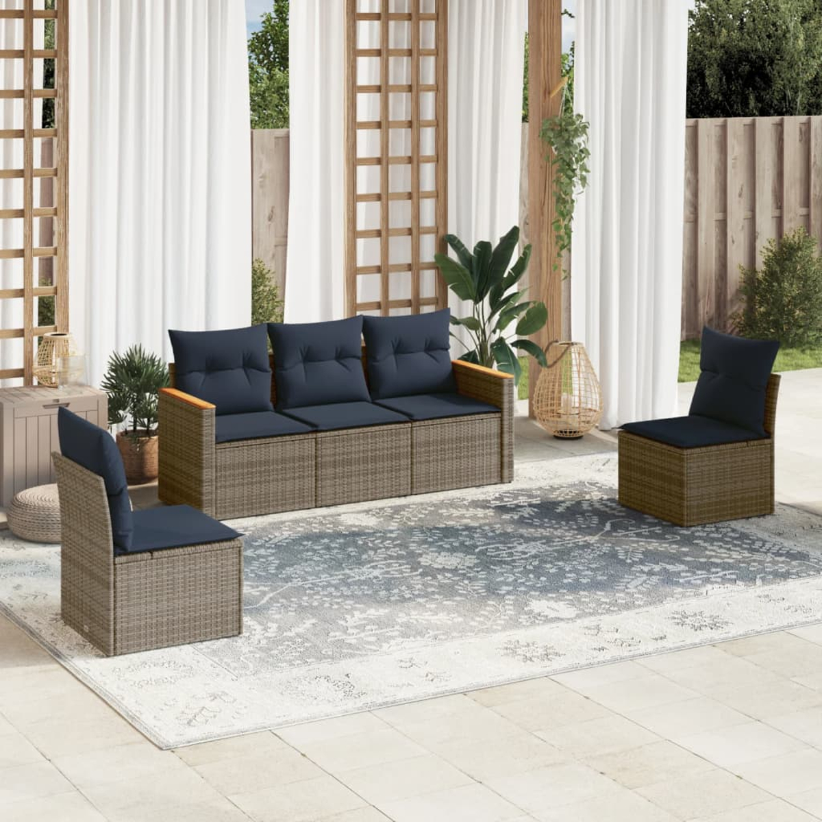 Garten-Sitzgruppe mit Sofa und Stühlen auf einem Teppich. Vorhänge und Pflanzen im Hintergrund. Die Möbel sind aus Korbgeflecht.