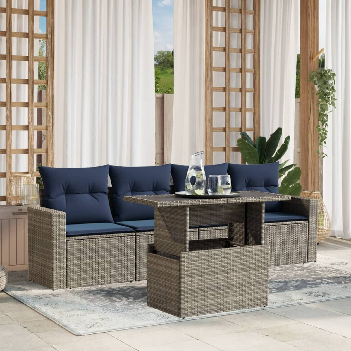 Gartenmöbel-Set mit blauen Kissen, einem Tisch mit Hubfunktion und weißen Vorhängen. Eine Kanne und Gläser stehen auf dem Tisch.