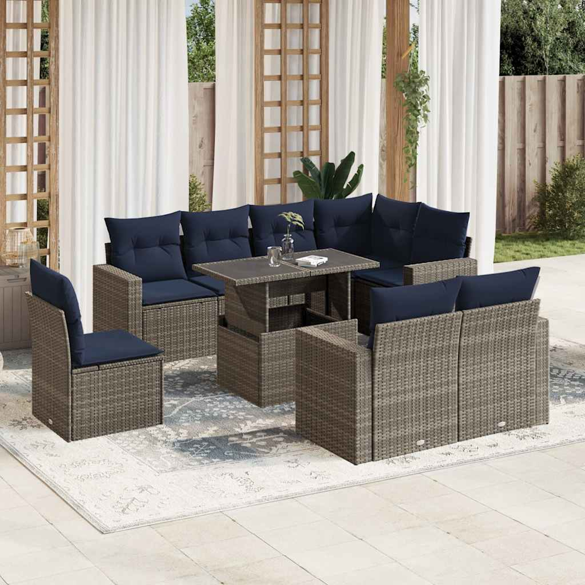 Gartenmöbel-Set mit grauem Korbgeflecht, marineblauen Kissen und einem Couchtisch. Die Szene umfasst einen Teppich, Vorhänge und einen Holzzaun.