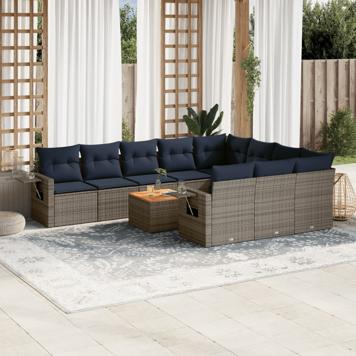 Outdoor-Ecksofa mit marineblauen Kissen, einem Holztisch und einem gemusterten Teppich auf einer Terrasse. Weiße Vorhänge und Holzrahmen im Hintergrund.