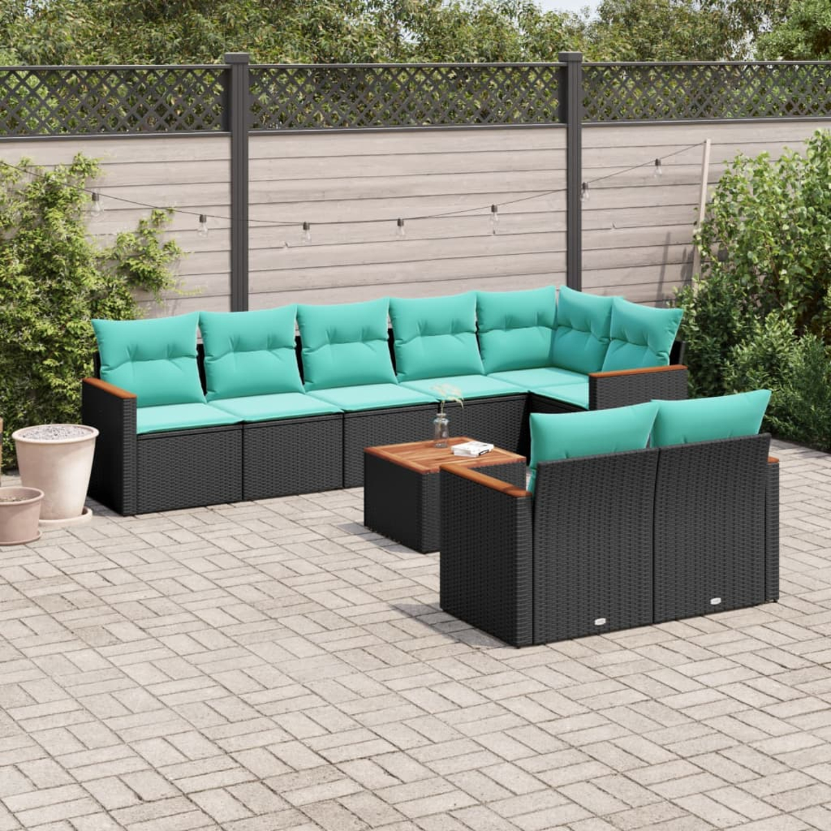 Terrassenset im Freien: schwarze Korbmöbel mit türkisfarbenen Kissen, Holztisch und grauer Zaun im Hintergrund.