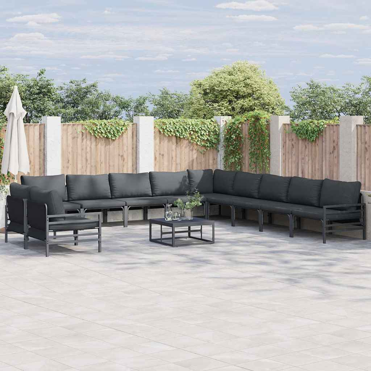 Outdoor-Ecksofa-Set mit grauen Kissen, Couchtisch und Sonnenschirm. Holzzaun und Grün im Hintergrund.