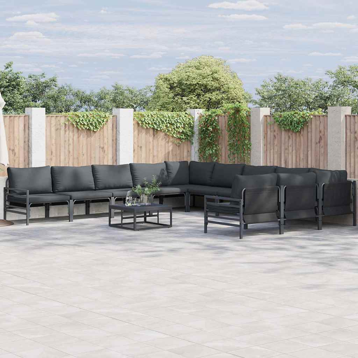 Terrassenset mit grauen Kissen. Beinhaltet Ecksofa, Sessel und Couchtisch, vor Holzzaun und Grün.