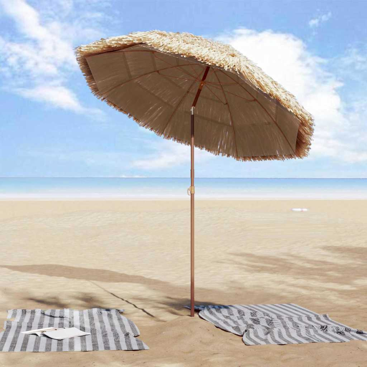 Strandszene mit Strohschirm, Handtüchern und Buch im Sand. Ozean und blauer Himmel sind im Hintergrund zu sehen.