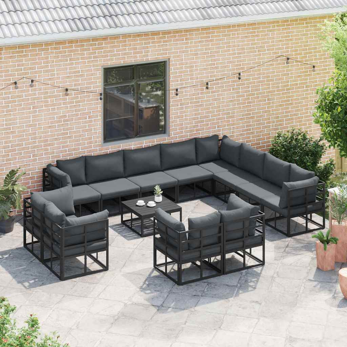 Set di sedute per esterni su un patio. Cuscini grigi e telai neri. Muro di mattoni e una finestra sullo sfondo.
