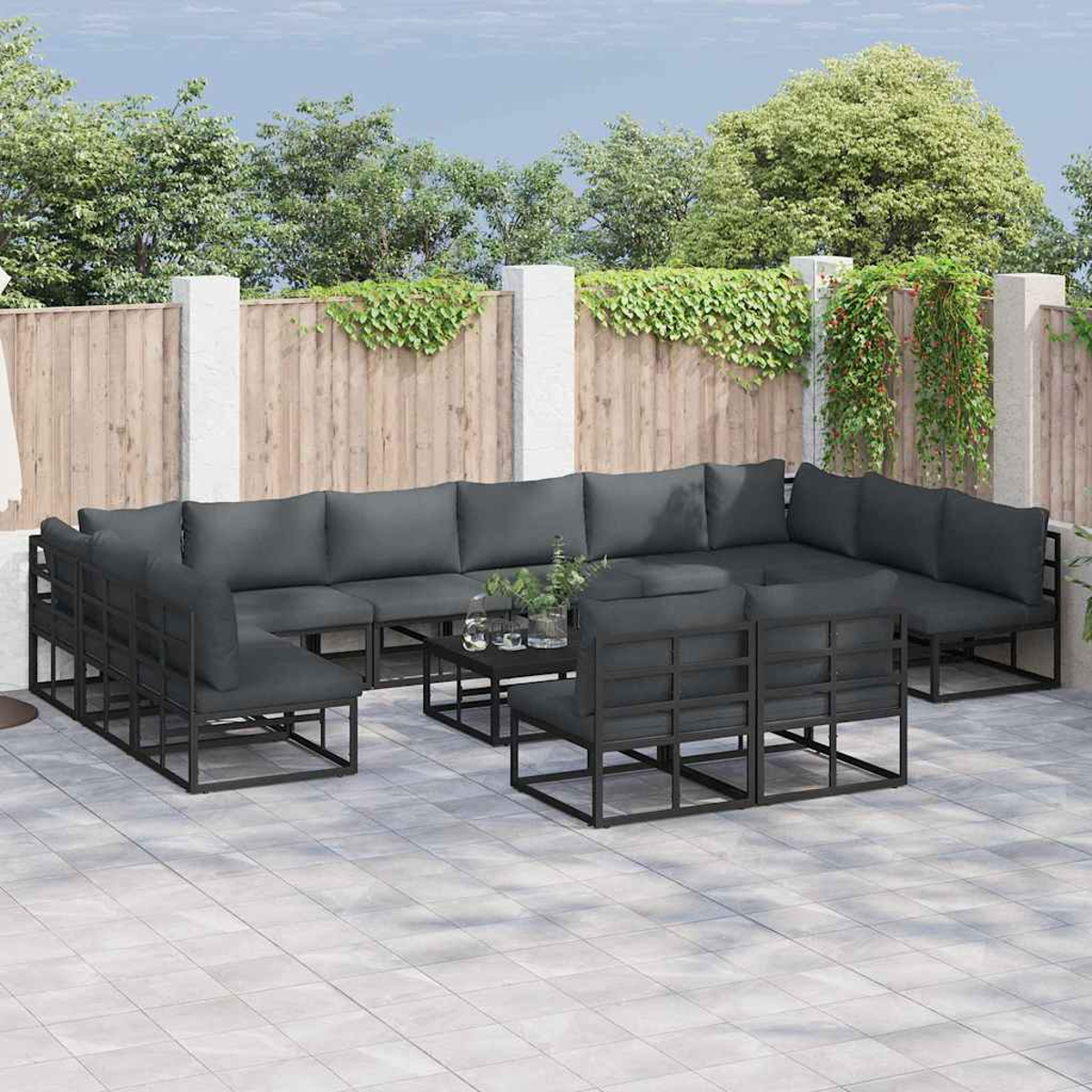 Garten-Lounge-Set mit dunkelgrauen Kissen und schwarzen Rahmen. Enthält ein Ecksofa, Stühle und einen Tisch auf einer gefliesten Terrasse.