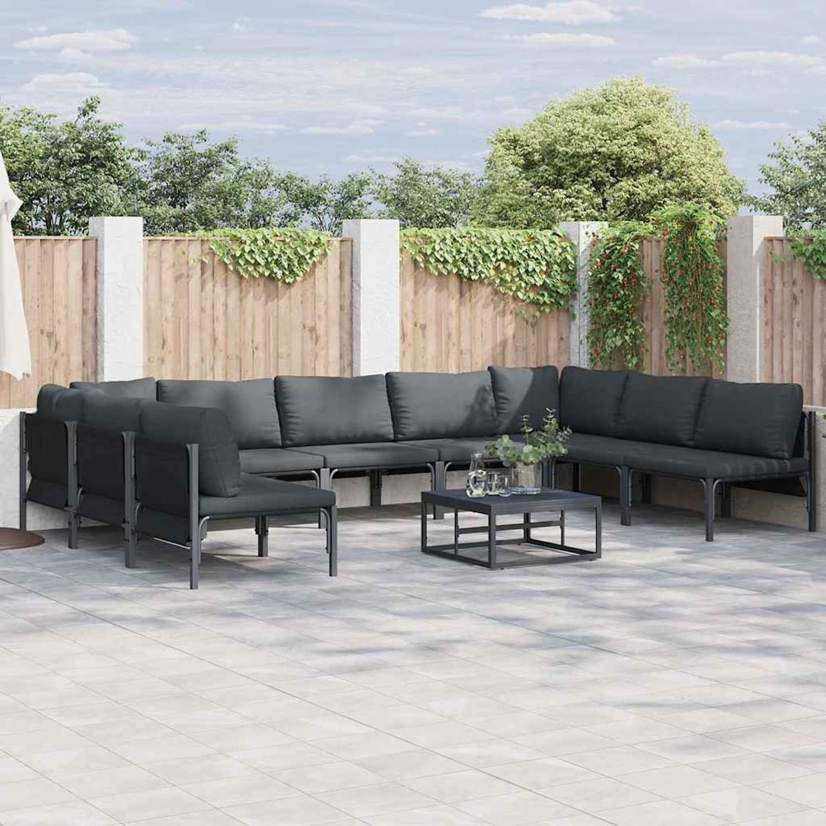 Outdoor-Ecksofa mit grauen Kissen und einem schwarzen Metallrahmen, angeordnet auf einer gefliesten Terrasse. Ein kleiner Tisch in der Mitte.