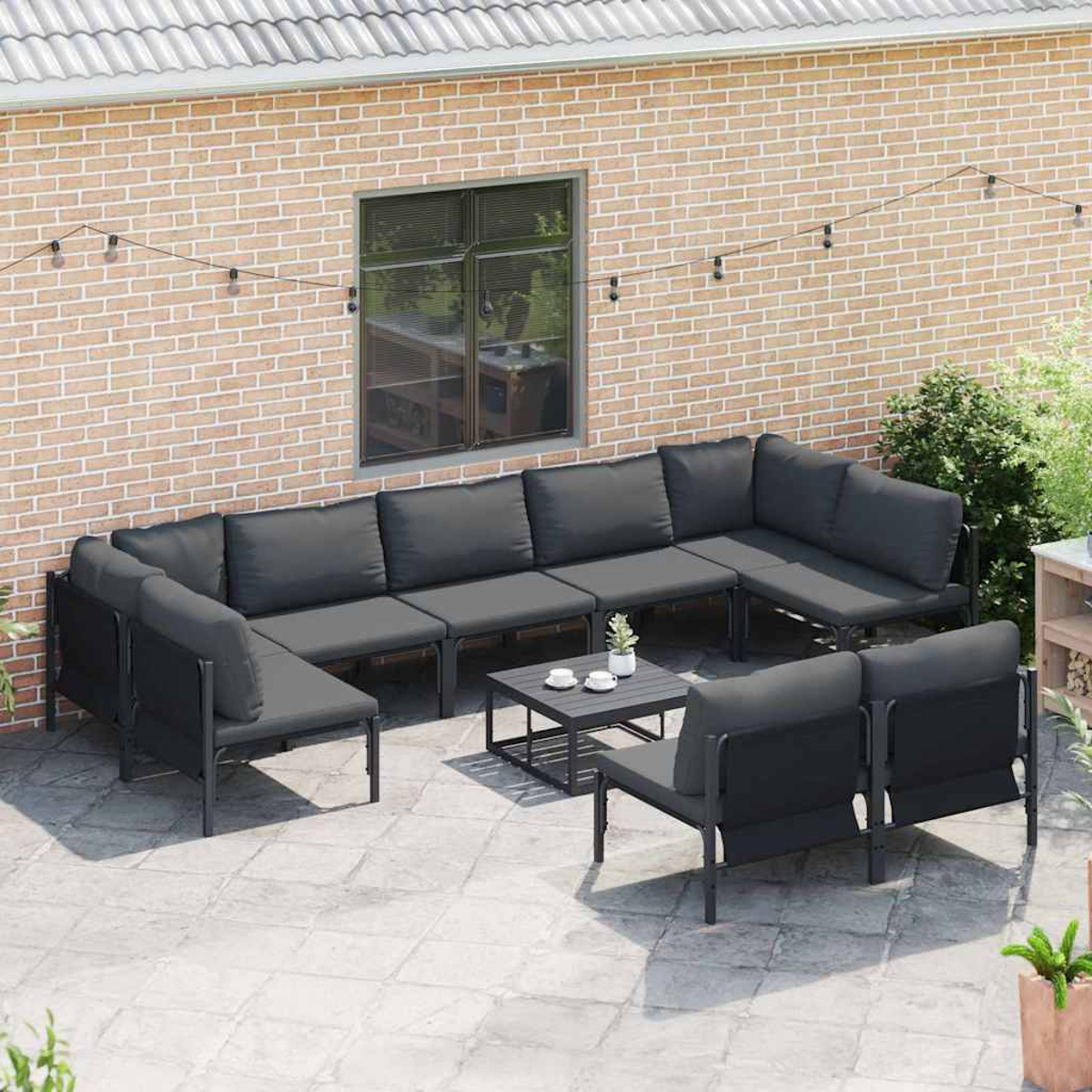 Garten-Terrassenset mit dunkelgrauen Kissen. Beinhaltet ein Ecksofa, zwei Stühle und einen Couchtisch auf einer Steinterrasse.
