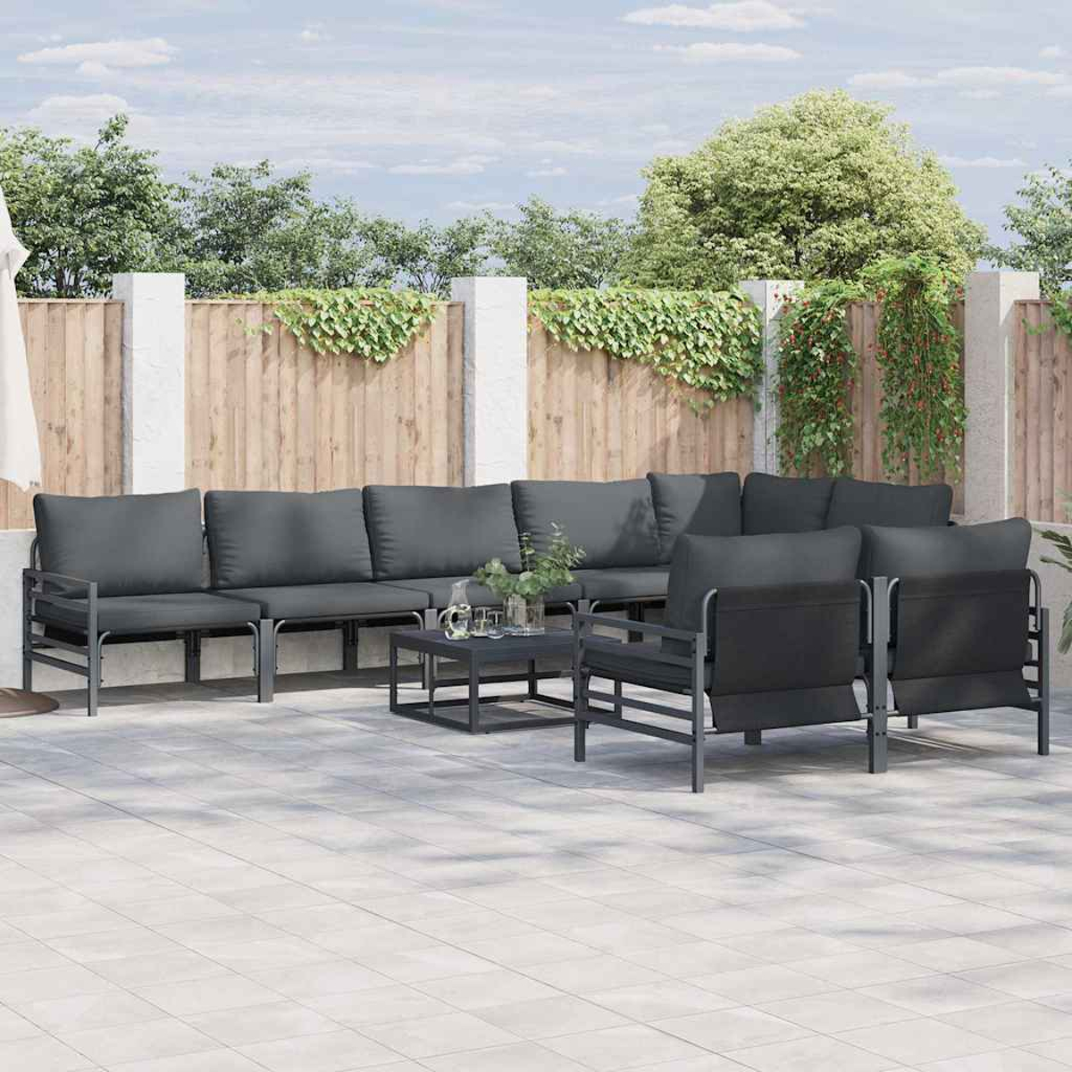 Gartenmöbel-Set mit grauen Kissen, Metallrahmen und einem kleinen Tisch auf einer gefliesten Terrasse. Holzzaun und Bäume im Hintergrund.