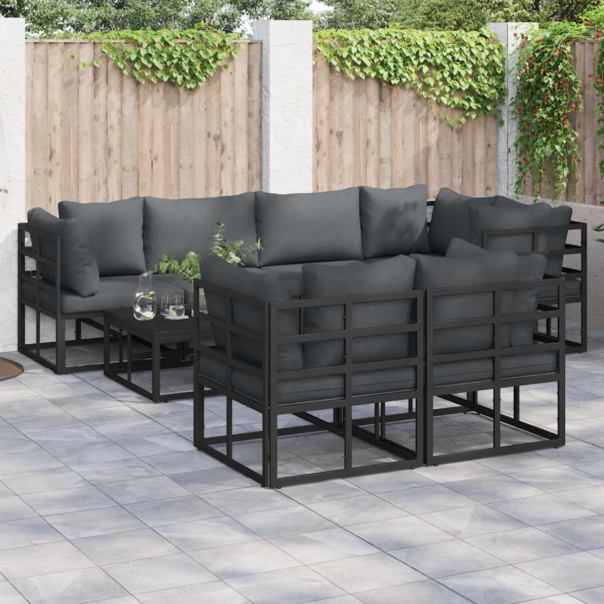 Outdoor-Sofa-Set mit grauen Kissen und einem schwarzen Tisch auf einer Terrasse. Holzzaun und Grün im Hintergrund.
