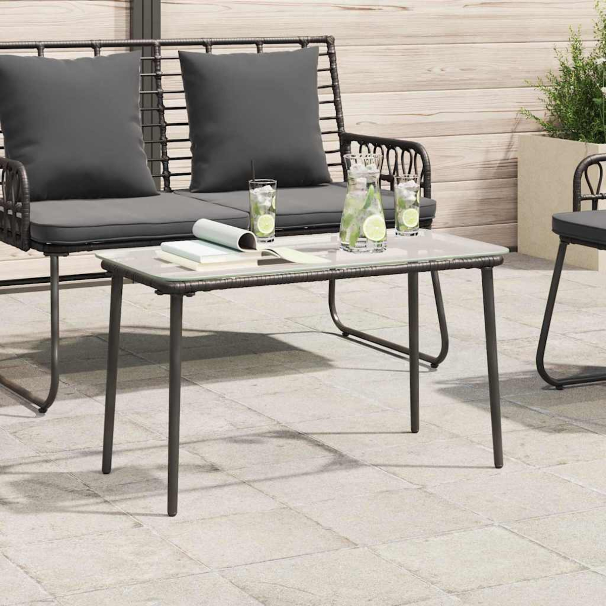 Eine Szene auf der Terrasse mit Tisch, Getränken und Sitzgelegenheiten. Ein Sofa mit grauen Kissen und ein kleiner Tisch mit Büchern und Gläsern.