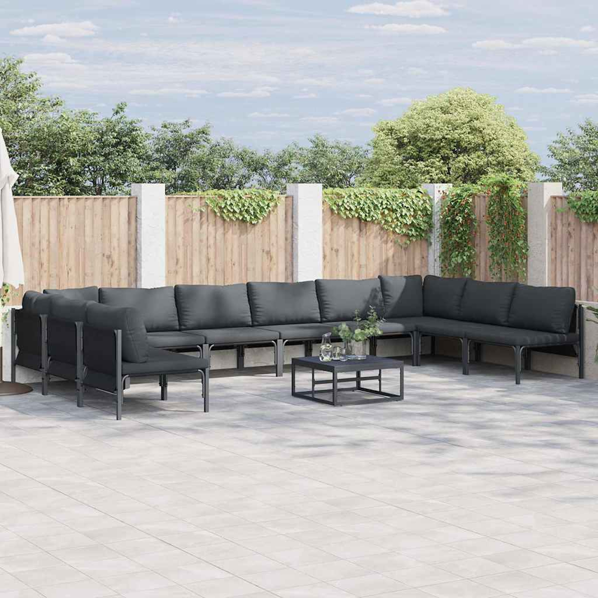 Divano componibile da esterno con cuscini grigi su un patio. Un tavolino quadrato davanti. Recinzione in legno e vegetazione sullo sfondo.