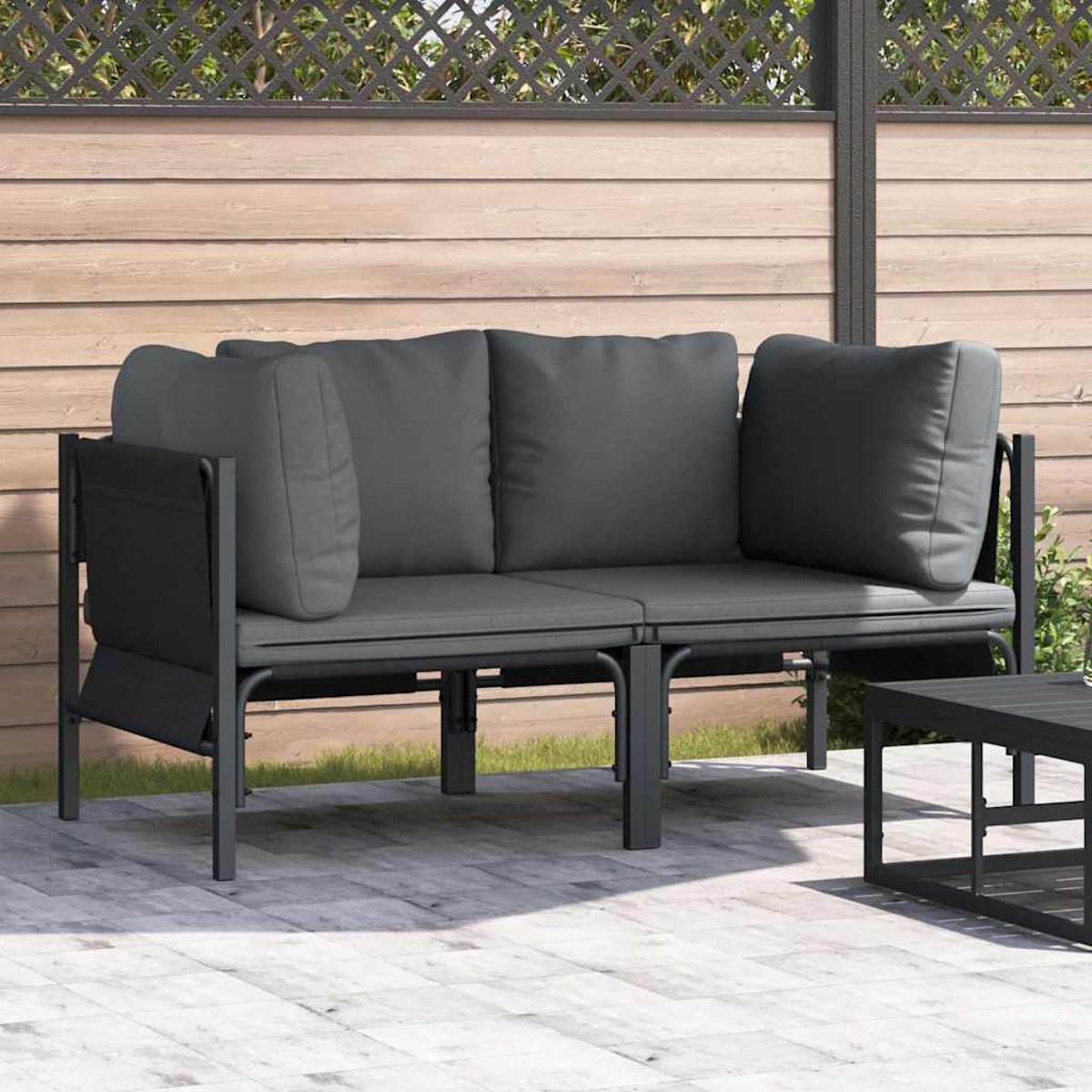 Ein graues Outdoor-Sofa mit Kissen steht auf einer Terrasse. Davor steht ein kleiner schwarzer Tisch. Ein Holzzaun befindet sich hinter dem Sofa.