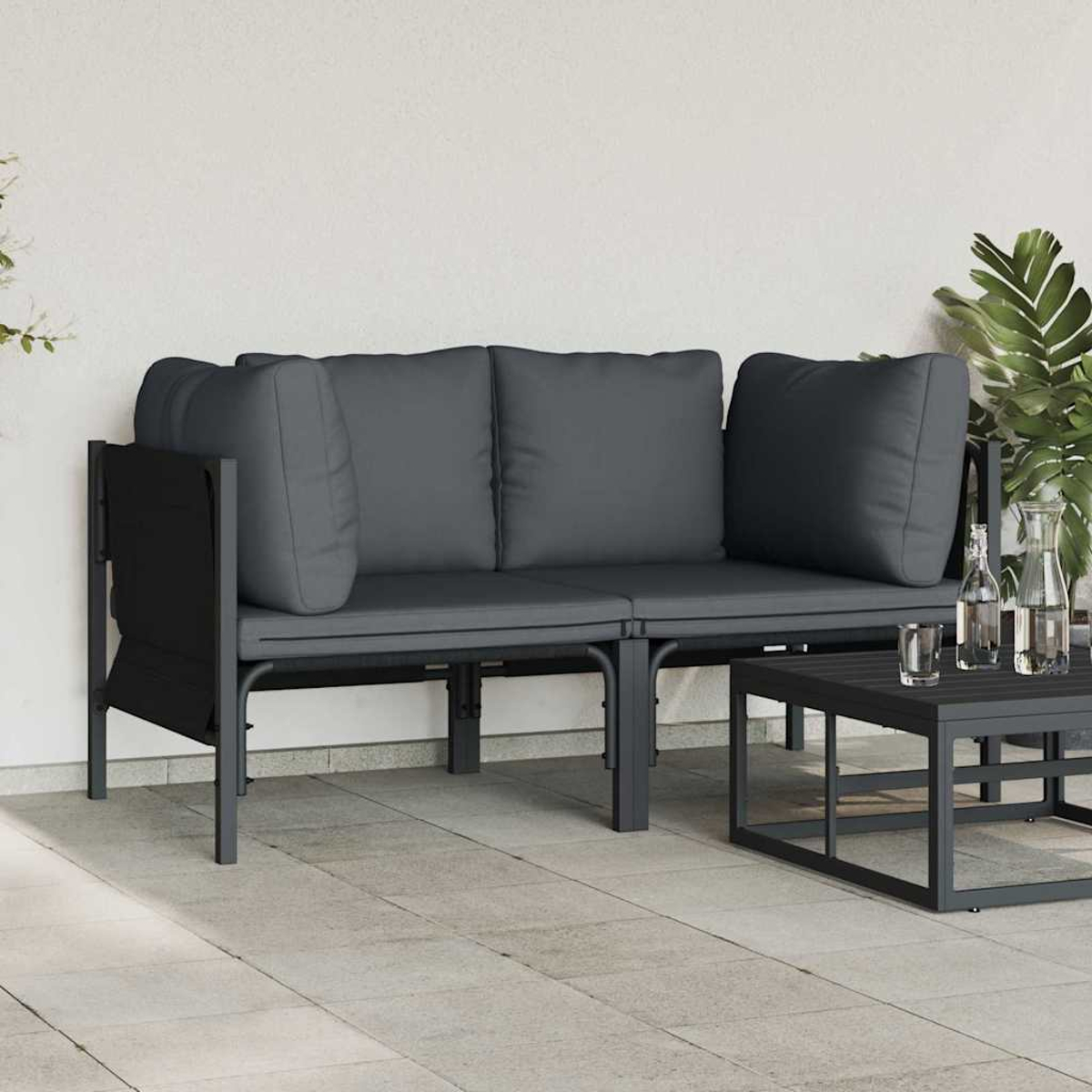 Außenszene mit grauem Sofa, Kissen und Couchtisch. Pflanzen und Wasserflaschen stehen auf dem Tisch auf einer Terrasse.