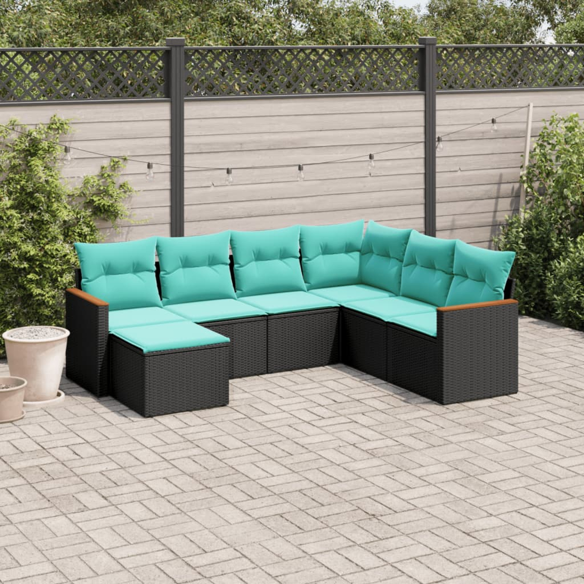Ein Ecksofa im Freien mit türkisfarbenen Kissen steht auf einer Terrasse. Im Hintergrund ein Zaun und Grün.
