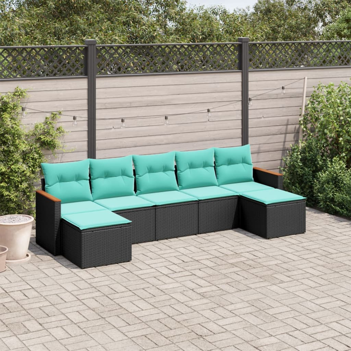 Outdoor-Ecksofa mit türkisfarbenen Kissen und schwarzem Korbboden auf einer gepflasterten Terrasse. Ein Zaun und Grün sind im Hintergrund.