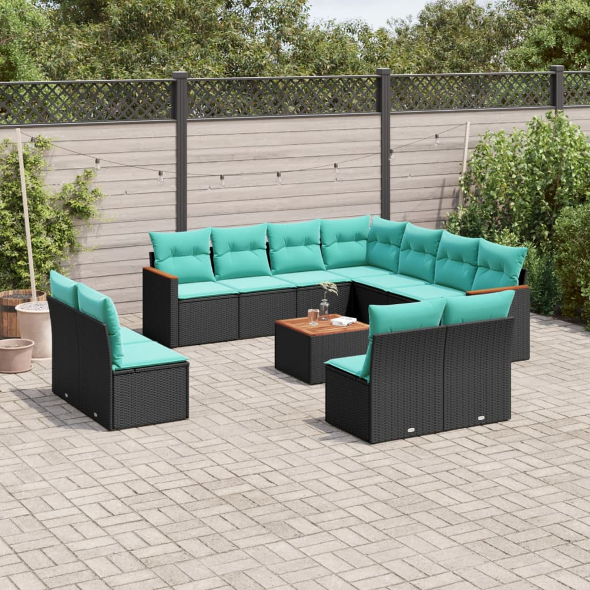 Gartenmöbel-Set: schwarze Korbflechtrahmen mit türkisfarbenen Kissen. Quadratischer Couchtisch. Ziegelterrasse, Holzzaun und grüne Blätter im Hintergrund.