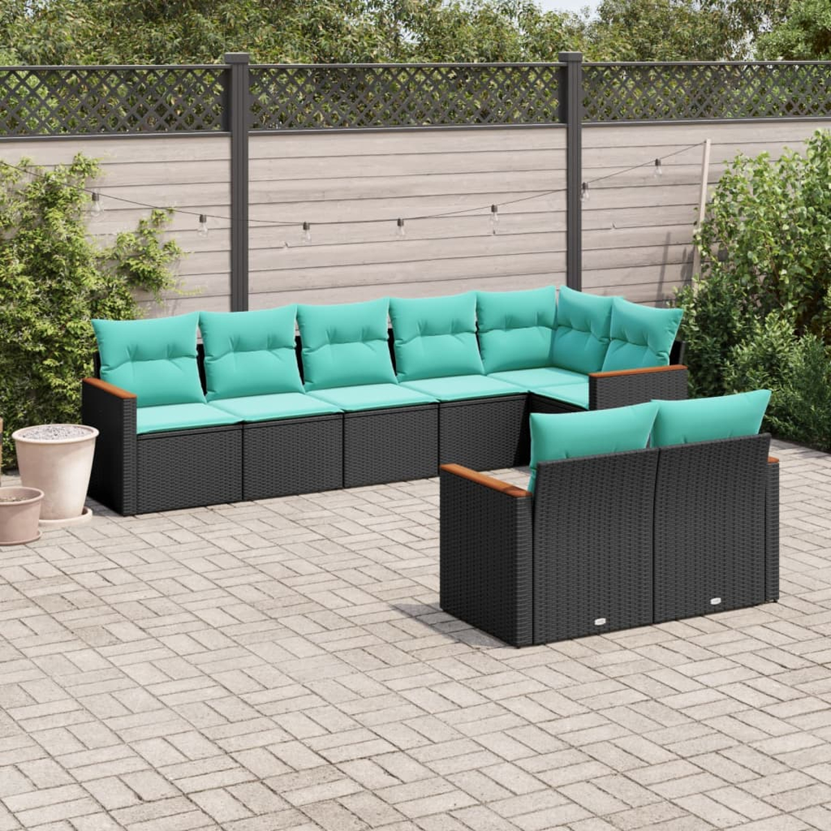 Juego de muebles de patio. Sofá de mimbre negro con cojines turquesa. Apoyabrazos de madera. Patio de ladrillos con valla de madera detrás.