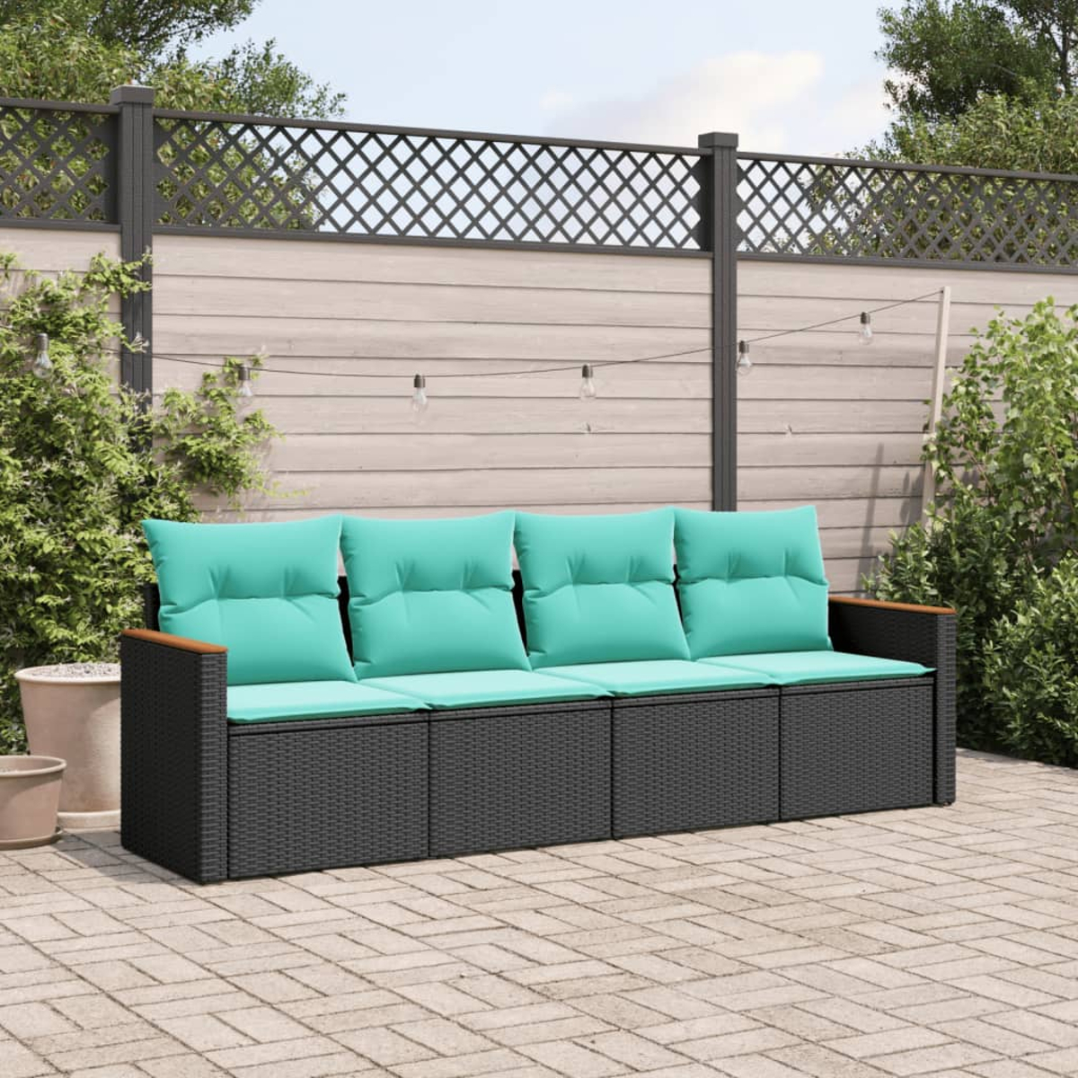 Un sofá negro de mimbre con cojines turquesa sobre un patio. Detrás, una valla de madera con celosía. Plantas verdes.
