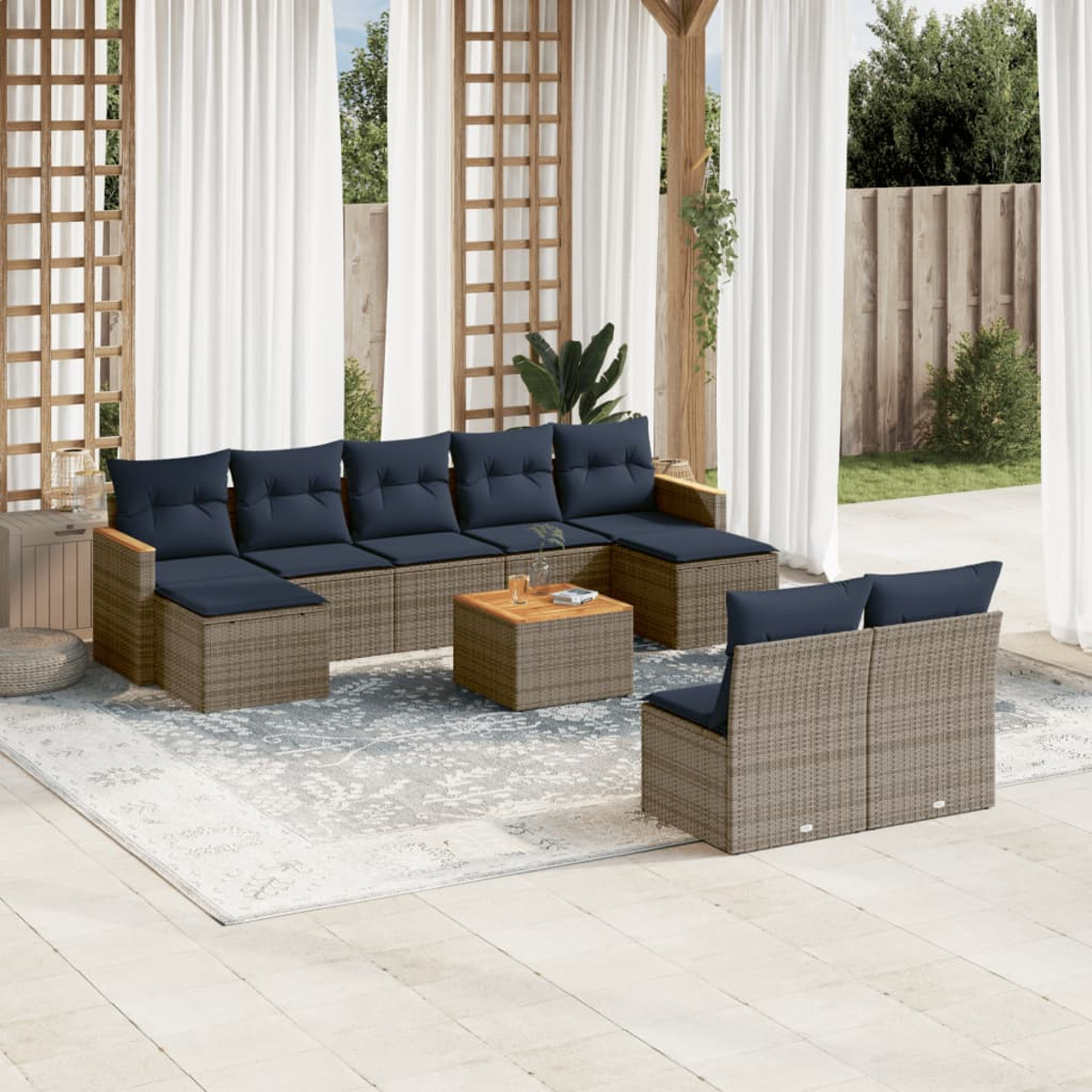 Terrassenset mit Rattan-Sofas und blauen Kissen. Ein Holztisch steht auf einem Teppich. Weiße Vorhänge und Grün im Hintergrund.