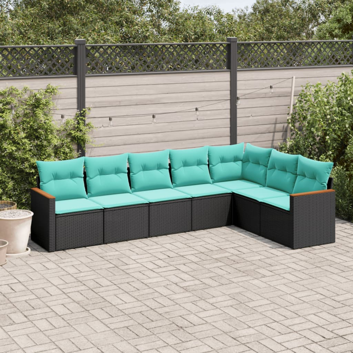 Ein Ecksofa im Freien mit türkisfarbenen Kissen steht auf einer Steinterrasse. Im Hintergrund sind ein Holzzaun und Grünflächen zu sehen.
